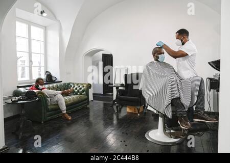 Barber wearing surgical mask and reusable gloves cutting hair of the customer Stock Photo