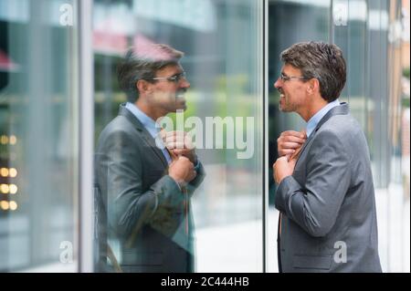 Businessman adjusting tie while looking at window in city Stock Photo