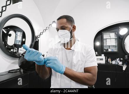 Barber wearing surgical mask putting on reusable gloves Stock Photo
