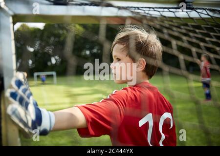 Serious boy in soccer uniform holding goal post at field Stock Photo