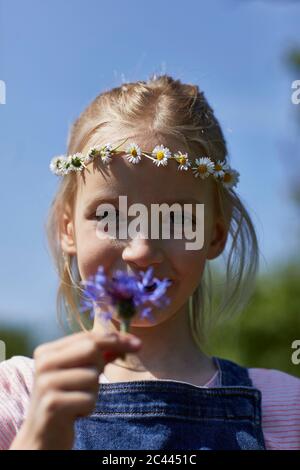 Portrait of girl wearing daisy wreath holding a flower