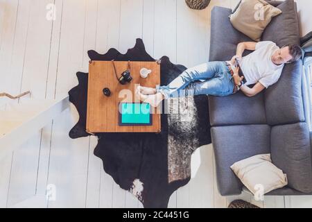 Directly above view of mid adult man relaxing while surfing net on digital tablet in living room at home Stock Photo