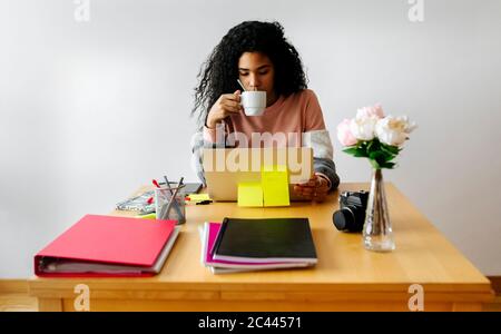 Young woman working from home using laptop and drinking coffee Stock Photo