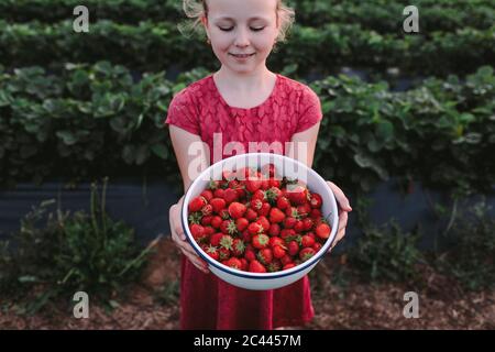 High angle view of smiling girl with fresh strawberries in bowl against plants