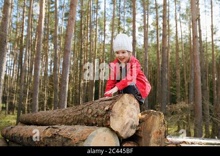 Portrait of happy little girl climbing on stack of wood in the forest Stock Photo