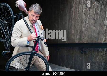 Businessman carrying bicycle while moving up on steps Stock Photo