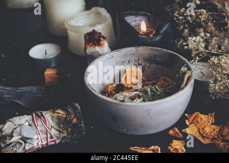 Close up of dried plants, herbs and yellow rose flower petals in a grey, dirty clay pot. Wiccan witch altar with ingredients for spell casting Stock Photo