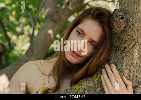 Thoughtful young woman looking away while leaning on tree trunk in garden Stock Photo