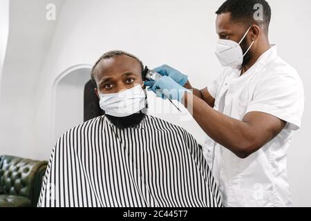 Barber wearing surgical mask and reusable gloves shaving hair of customer Stock Photo
