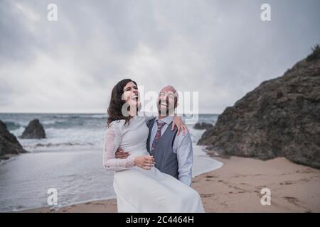 Laughing bridal couple at the beach, holding his wife Stock Photo