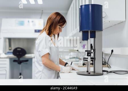 Confident mature female healthcare worker writing data at laboratory desk Stock Photo