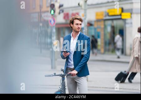 Portrait of young businessman with bicycle and smartphone waiting in the city Stock Photo