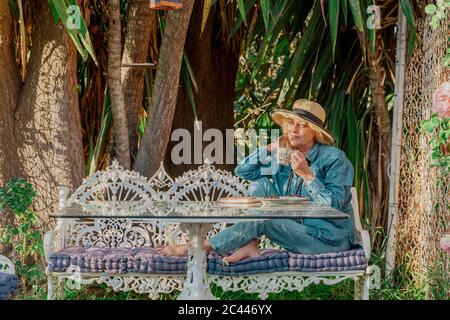 Senior woman sitting on garden bench drinking cup of tea Stock Photo