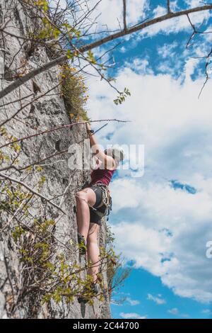 Determined young woman moving up while rock climbing against sky Stock Photo
