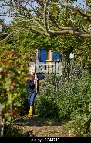 Girl in allotment garden carrying tools Stock Photo