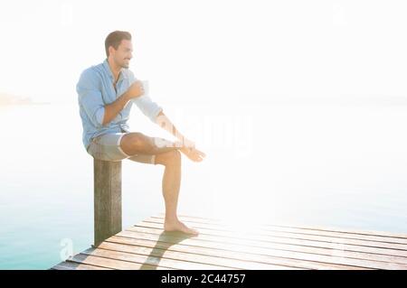 Young man relaxing with cup of coffee on jetty Stock Photo