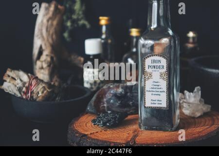 Close up of bottle of iron dust powder with vintage apothecary label on witch altar. Various spell ingredients in background - glass jars bottles sage Stock Photo