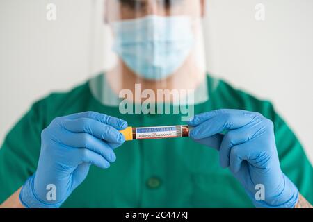 Man in protective wear holding positive covid-19 test Stock Photo