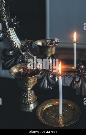 Mirror magick witchcraft - scrying with a white lit burning candle to read the flame. A reflection in a dark, moody brass gold colored vintage mirror Stock Photo