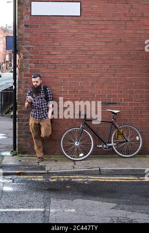 Bearded mid adult man using smart phone while standing against brick wall Stock Photo