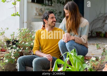 Happy couple talking while sitting on steps against farmhouse Stock Photo