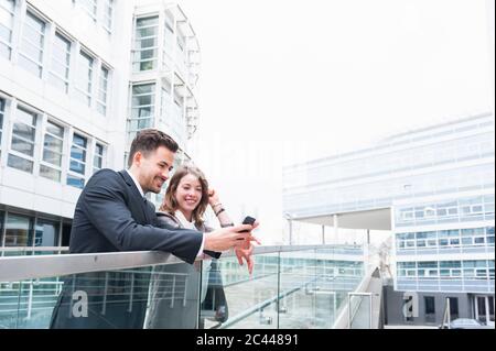Business couple using smart phone on elevated walkway outside office building Stock Photo