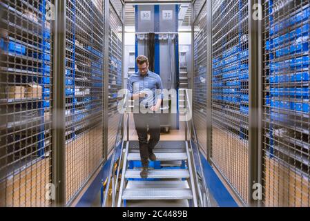 Businessman using smartphone walking down stairs in a factory Stock Photo