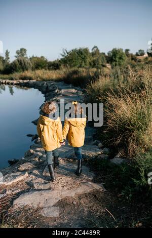 Siblings holding hands while walking on rocks at riverbank Stock Photo