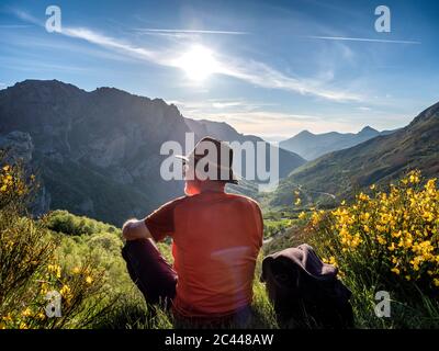 Rear view of senior man sitting on mountain against sky, Alto de La Farrapona, Asturias, Spain Stock Photo