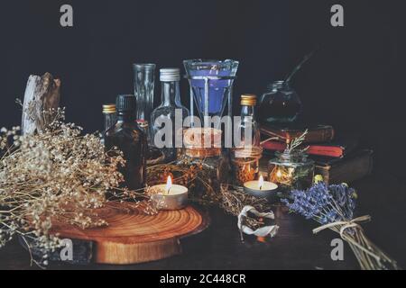 Wiccan witch apothecary - various ingredients, potions and dried herb bottles, jars for magick, placed on an altar. Dark, black background Stock Photo