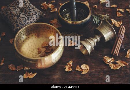 Tibetan themed close up with examples of two different singing bowls - a dark brown, and gold colored one, and antique looking incense holder
