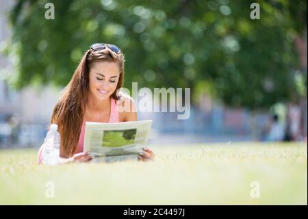 Portrait of smiling woman lying on a meadow reading newspaper Stock Photo