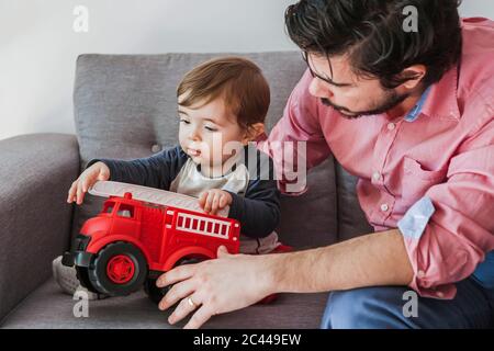 Baby boy sitting on couch with his father playing with fire engine toy car Stock Photo