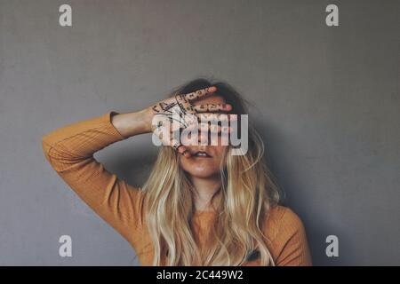 Palmistry themed portrait of young blond female wiccan witch placing her painted hand on her face and eyes. Dark, moody filter, mustard yellow shirt Stock Photo