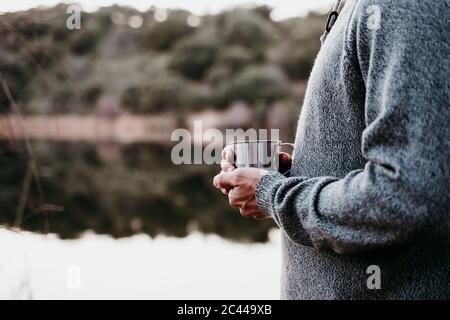 Close-up of man holding mug at lakeside Stock Photo