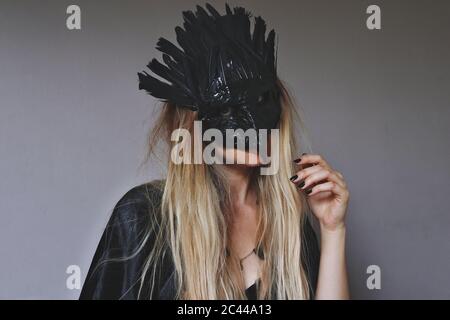 Young female wiccan witch wearing a Samhain hand made raven mask witch black feather crown. Blond woman wearing a black dress in a Halloween mask Stock Photo