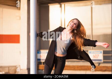 Beautiful young woman swinging around metallic pole in city Stock Photo