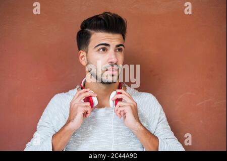 Young handsome man holding headphones against brown wall Stock Photo