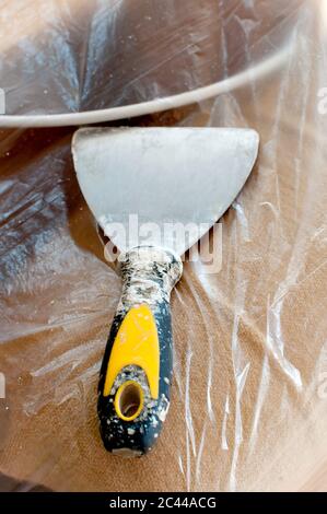 old dirty scraper on transparent plastic foil, preparations for painting house, close up Stock Photo