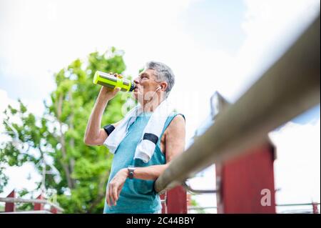 Low angle view of thirsty senior man drinking water from bottle while leaning on railing at park Stock Photo