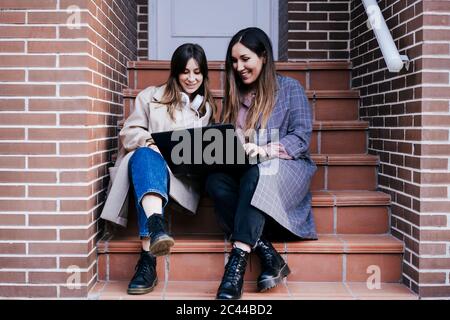 Portrait of two women sitting on stairs outdoors looking at laptop Stock Photo