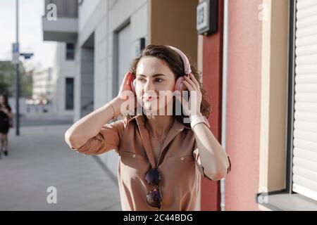 Thoughtful businesswoman listening music through headphones during sunny day