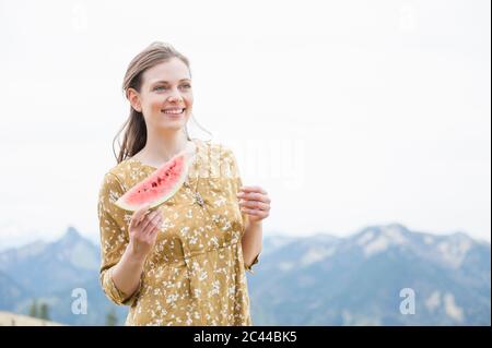 Beautiful smiling woman holding watermelon slice while standing against sky Stock Photo