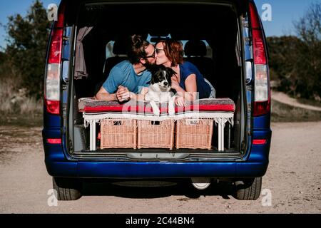 Couple with dog kissing in the boot of a minivan Stock Photo