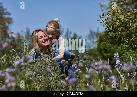 Happy mother carrying daughter piggyback in allotment garden Stock Photo