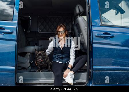 Portrait of smiling woman sitting with her bulldog in van Stock Photo