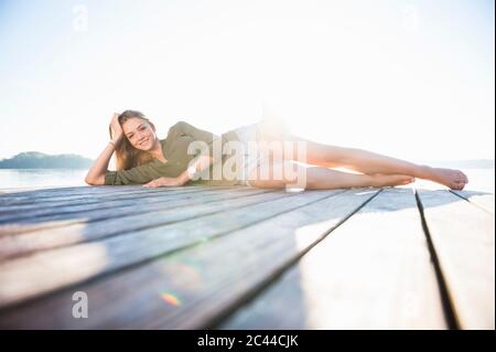 Portrait of smiling young woman lying on jetty at backlight Stock Photo