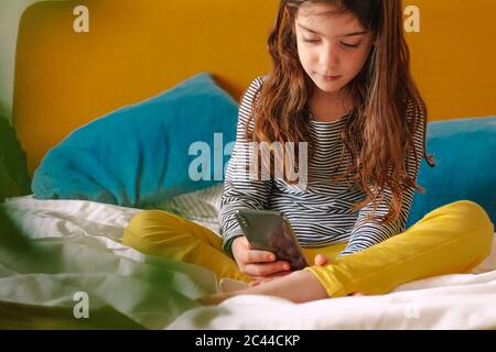 Girl using smartphone sitting on bed Stock Photo