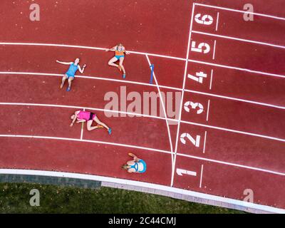 Germany, Baden Wurttemberg, Winterbach, Aerial view of three female sprinters resting on track right past finish line Stock Photo