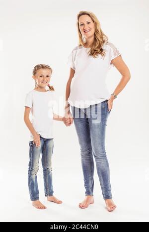 Portrait of happy pregnant woman  standing hand in hand with her daughter in front of white background Stock Photo